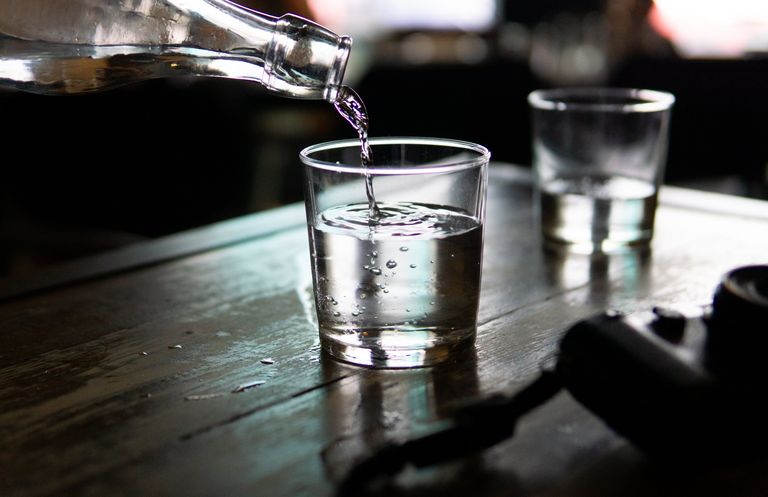 Water being poured from a glass bottle into a short glass